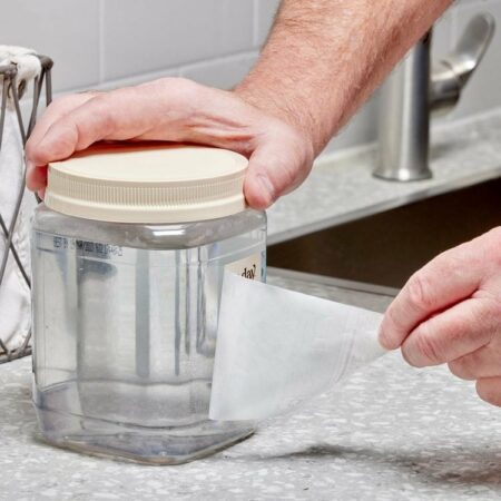 Une personne décolle une étiquette d'un bocal transparent dans une cuisine.