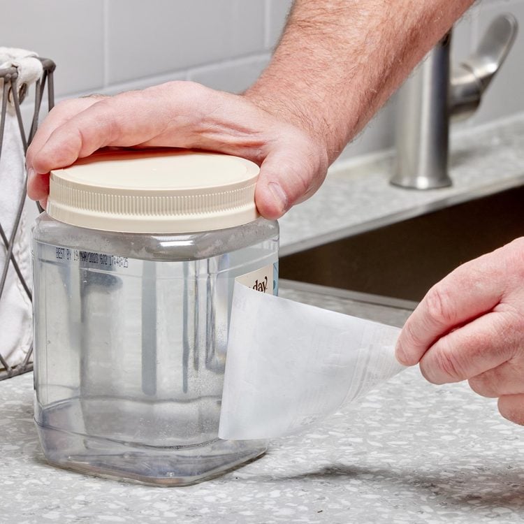 Une personne décolle une étiquette d'un bocal transparent dans une cuisine.