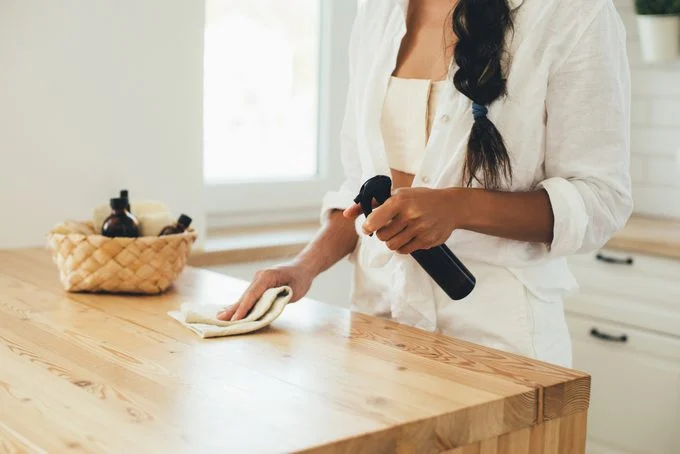Femme en train de nettoyer une table en bois avec un spray et un chiffon.