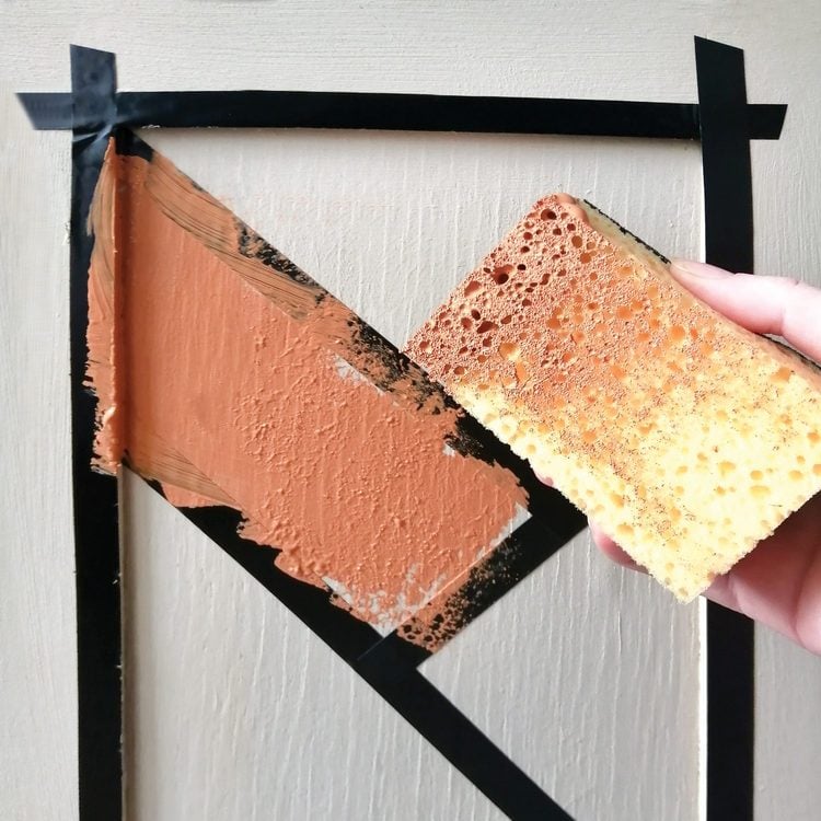 Une main utilise une éponge pour tamponner de la peinture orange sur un meuble.