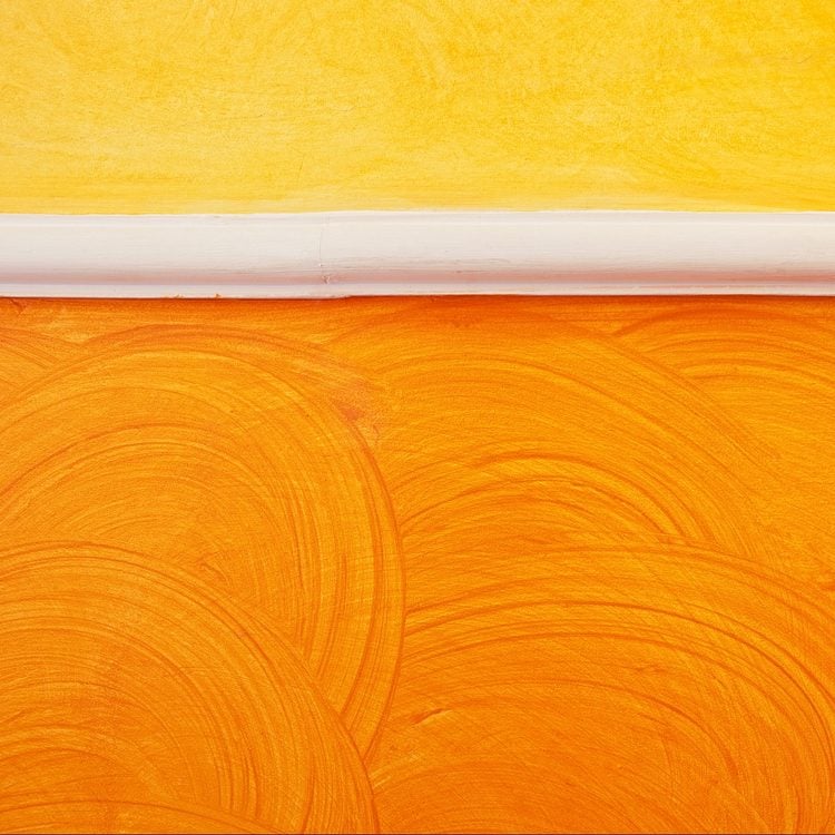 Un mur peint en jaune avec une plinthe blanche, créant un effet de couleur texturé.