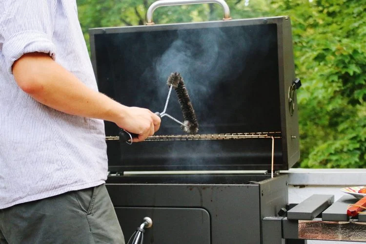 Un homme qui nettoie une grille de barbecue avec une brosse