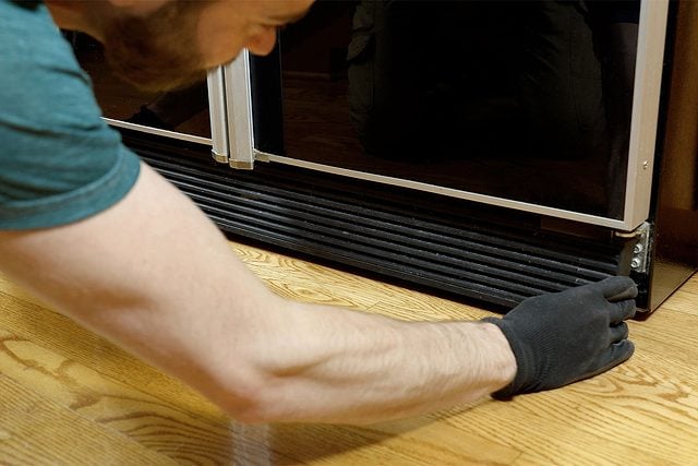 Une personne dévisse la grille de protection à l'arrière d'un frigo.