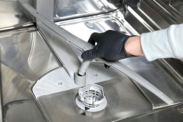Une main dévisse le bras de lavage inférieur du lave-vaisselle.