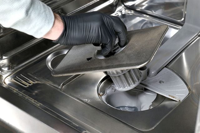 Une main dévisse et retire le filtre cylindrique du fond du lave-vaisselle.