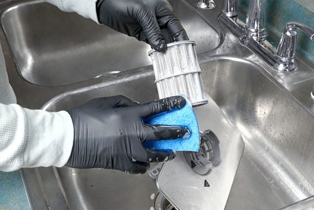 Une personne nettoie le filtre du lave-vaisselle avec une brosse sous l'eau courante.