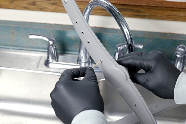 Une personne utilise un cure-dent pour déboucher les trous d'un bras de lavage.