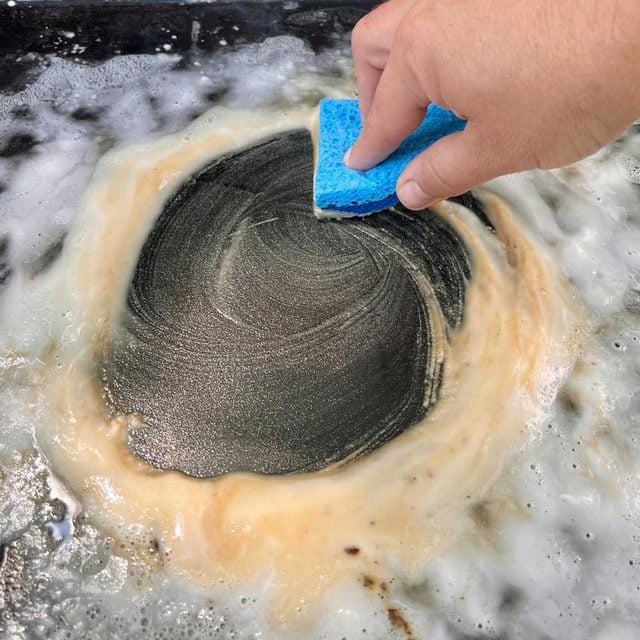Une main frotte la plancha avec une éponge.