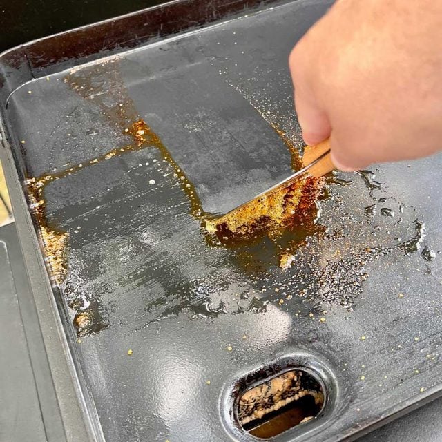 Une main utilise une spatule pour gratter la surface d'une plancha.