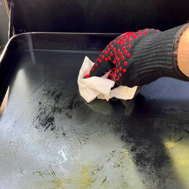 Une main gantée essuie une plaque de cuisson avec du papier absorbant.