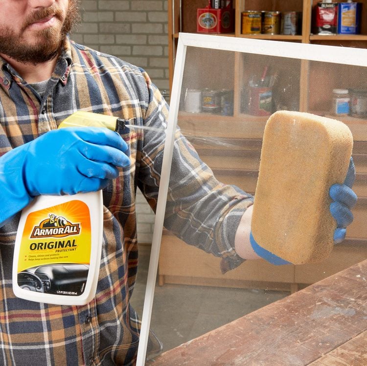 Une personne gantée pulvérise un produit sur une moustiquaire tout en tenant une éponge.