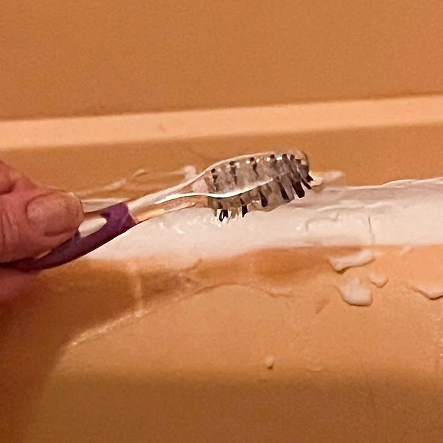 Application de la pâte sur les joints de douche moisis avec une brosse à dents.