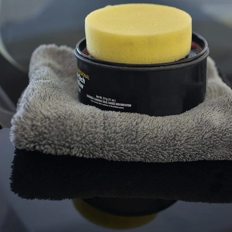 Une boîte de cire pour voiture noire avec une éponge jaune sur un chiffon en microfibre.