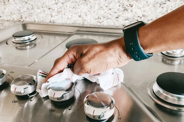 main nettoyant les boutons d'une cuisinière en inox avec un chiffon