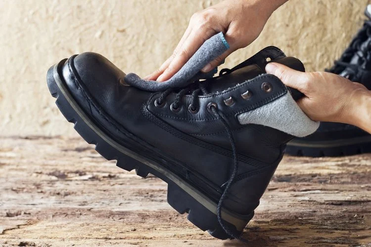 main nettoyant une botte en cuir noir avec un chiffon gris