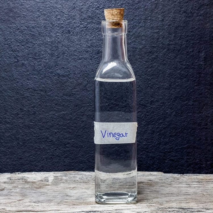 Une bouteille en verre de vinaigre avec un bouchon en liège sur une table en bois.