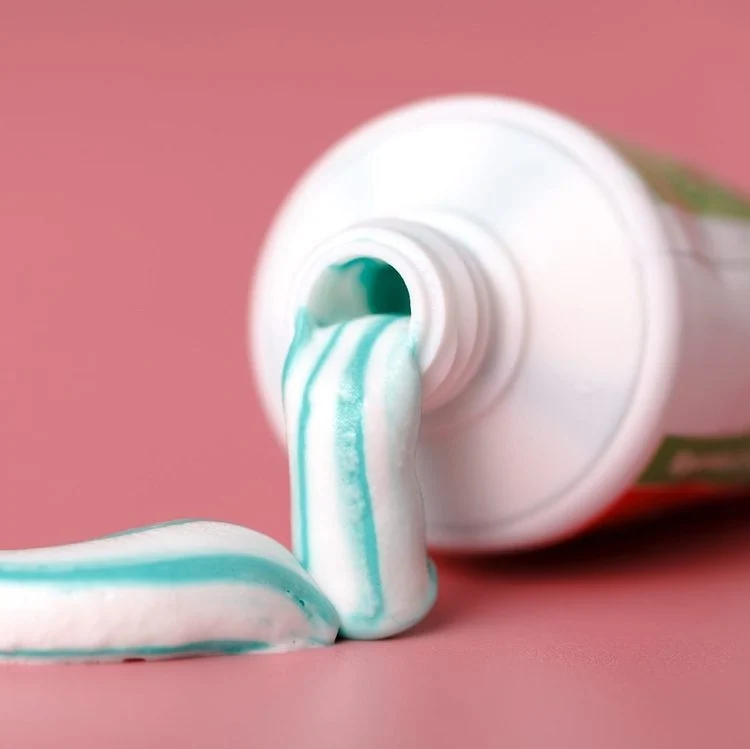 Un tube de dentifrice pressé sur une surface rose.