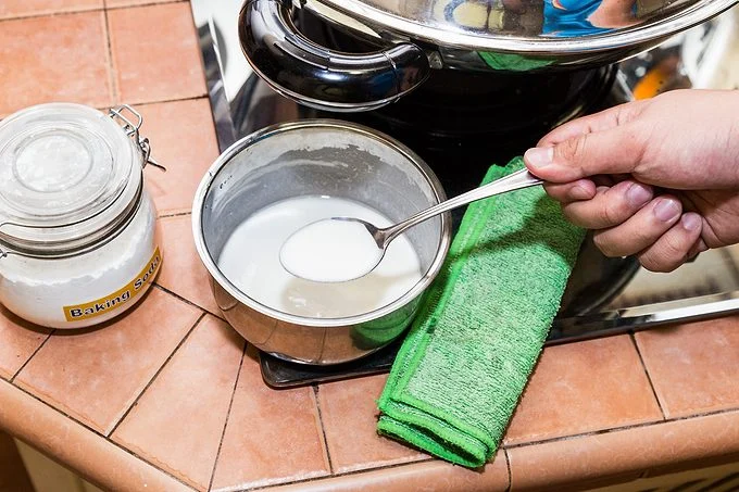 Une main mélange du bicarbonate de soude et de l'eau dans un bol.