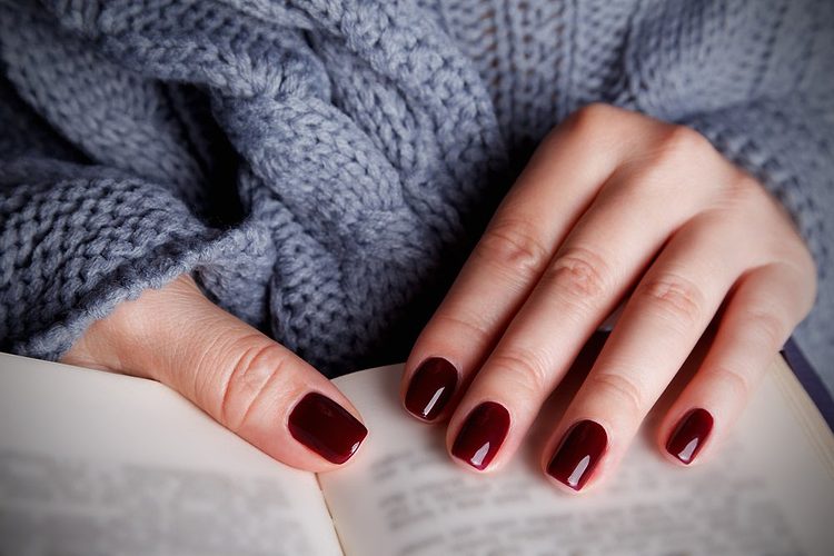 Des mains avec du vernis rouge tenant un livre.
