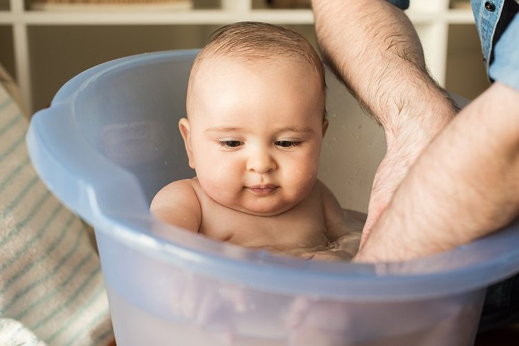 Un parent lavant son bébé dans une petite baignoire.