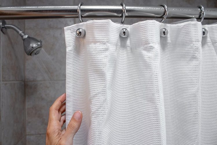 Une main tire un rideau de douche blanc.