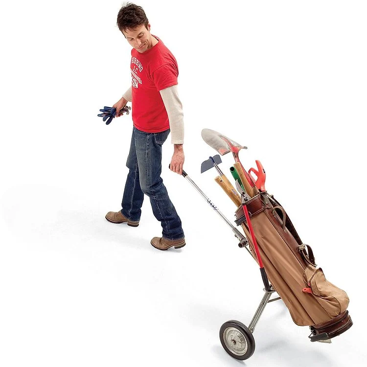 Un homme tire un chariot de golf rempli d'outils de jardin.