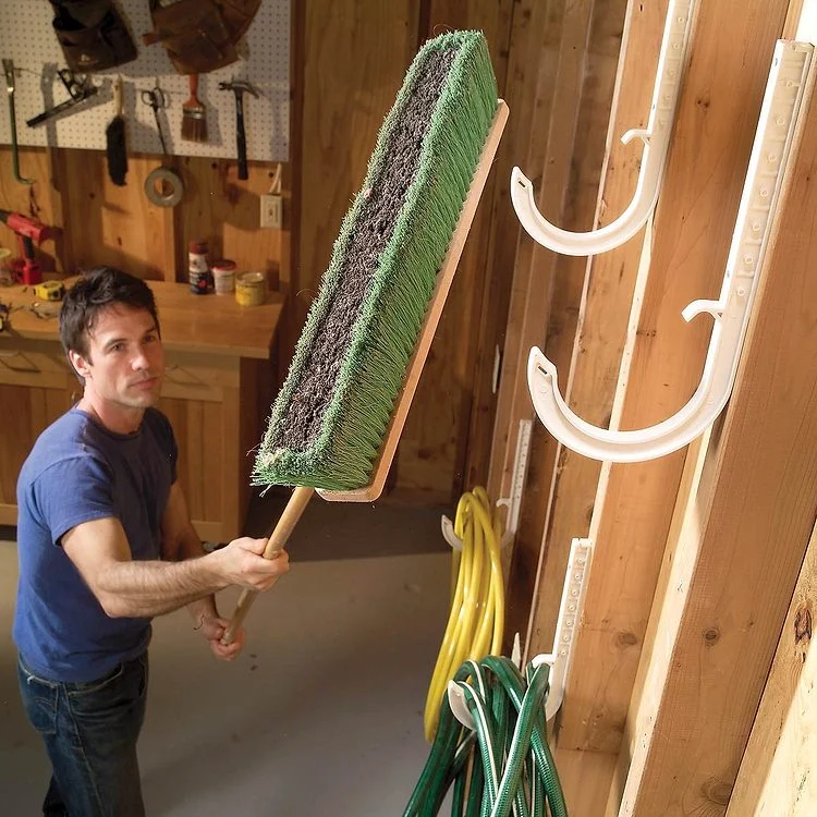 Un homme nettoie son garage bien organisé avec des outils suspendus au mur.