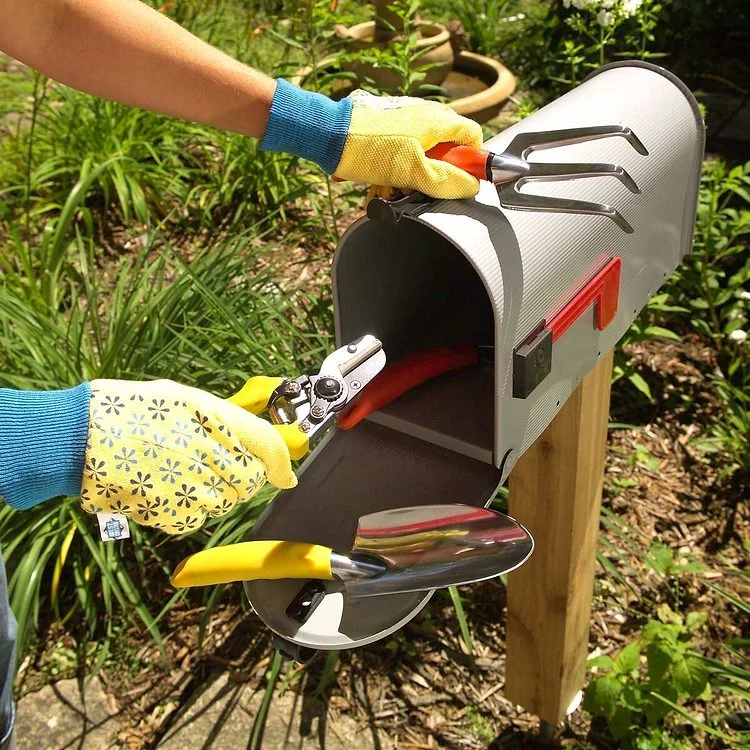 Une personne ouvre une boîte aux lettres installée dans le jardin pour y prendre ses outils.