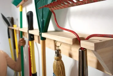 Des outils de jardin suspendus à un râtelier mural en bois.