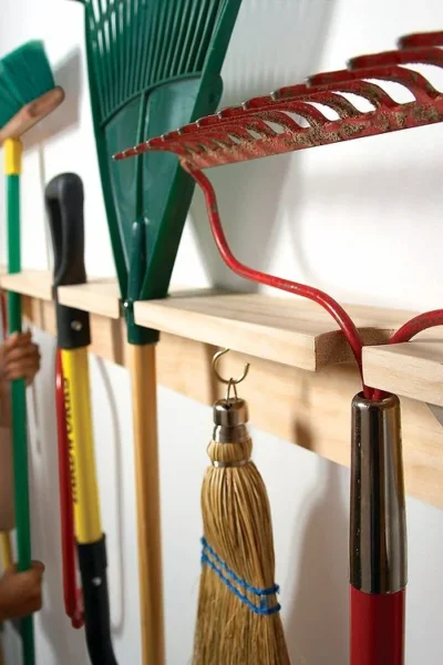 Des outils de jardin suspendus à un râtelier mural en bois.