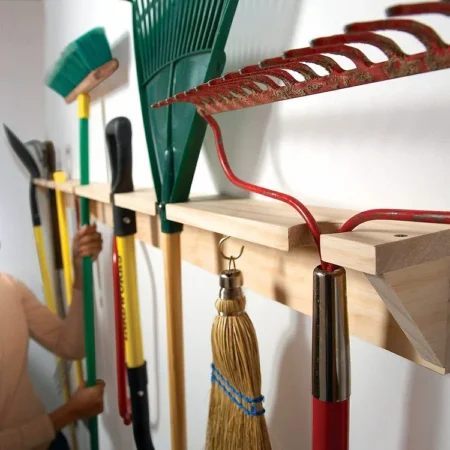 Des outils de jardin suspendus à un râtelier mural en bois.