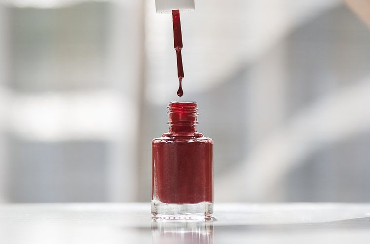 Un flacon de vernis à ongles rouge avec le pinceau.